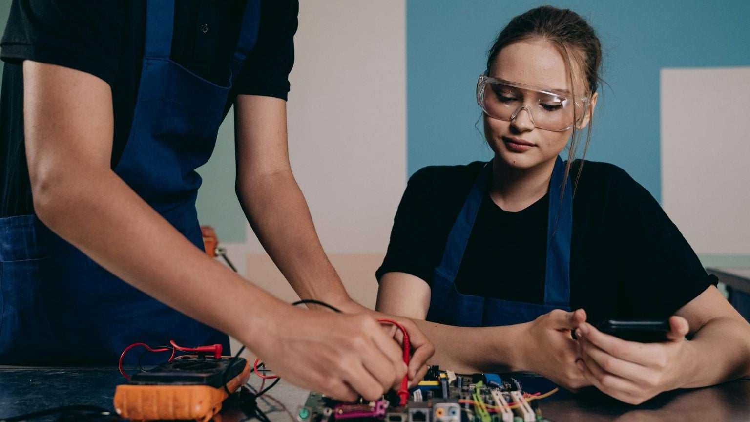 A young women with another student testing wires using a voltage tester.